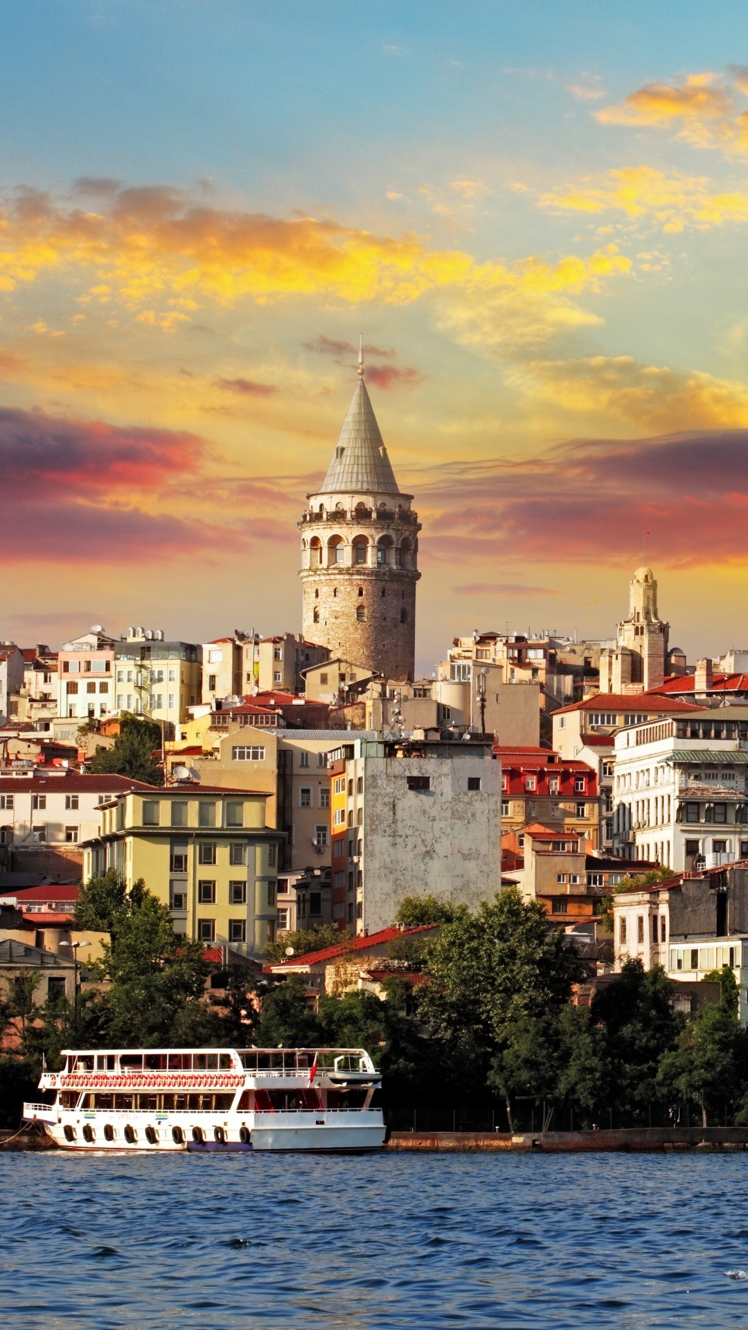 Galata Tower at sunset in Istanbul, Turkey, with the colorful cityscape and a passenger ferry on the Bosphorus