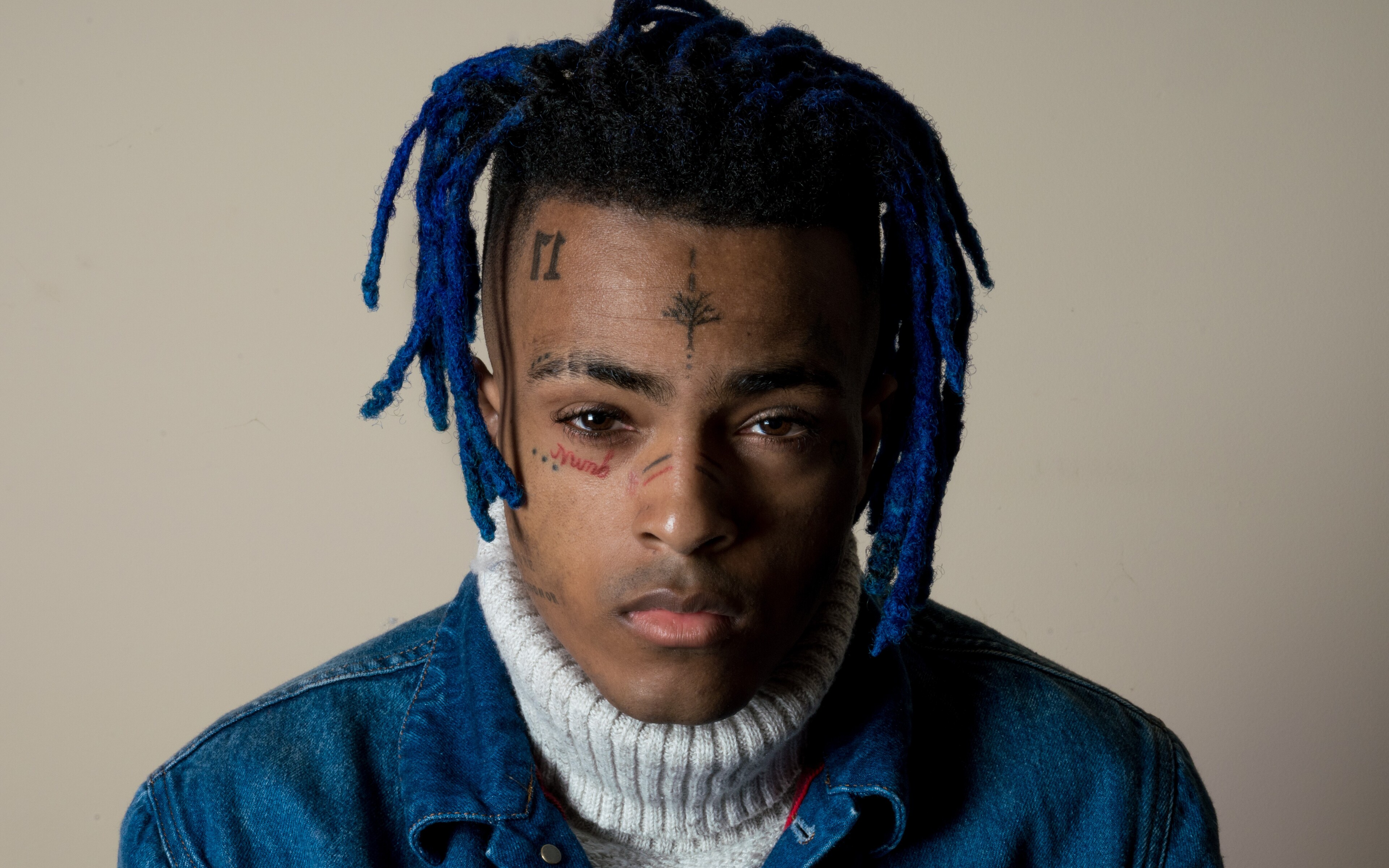 Close-up portrait of XXXTentacion with blue dreadlocks, wearing a denim jacket and a turtleneck