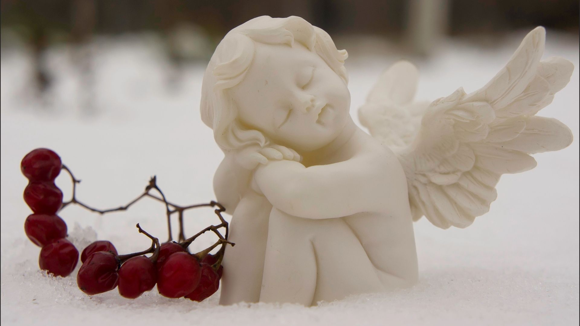 A serene snow angel figurine rests peacefully in the snow, adorned with red berries, evoking a sense of tranquility and winter's gentle beauty