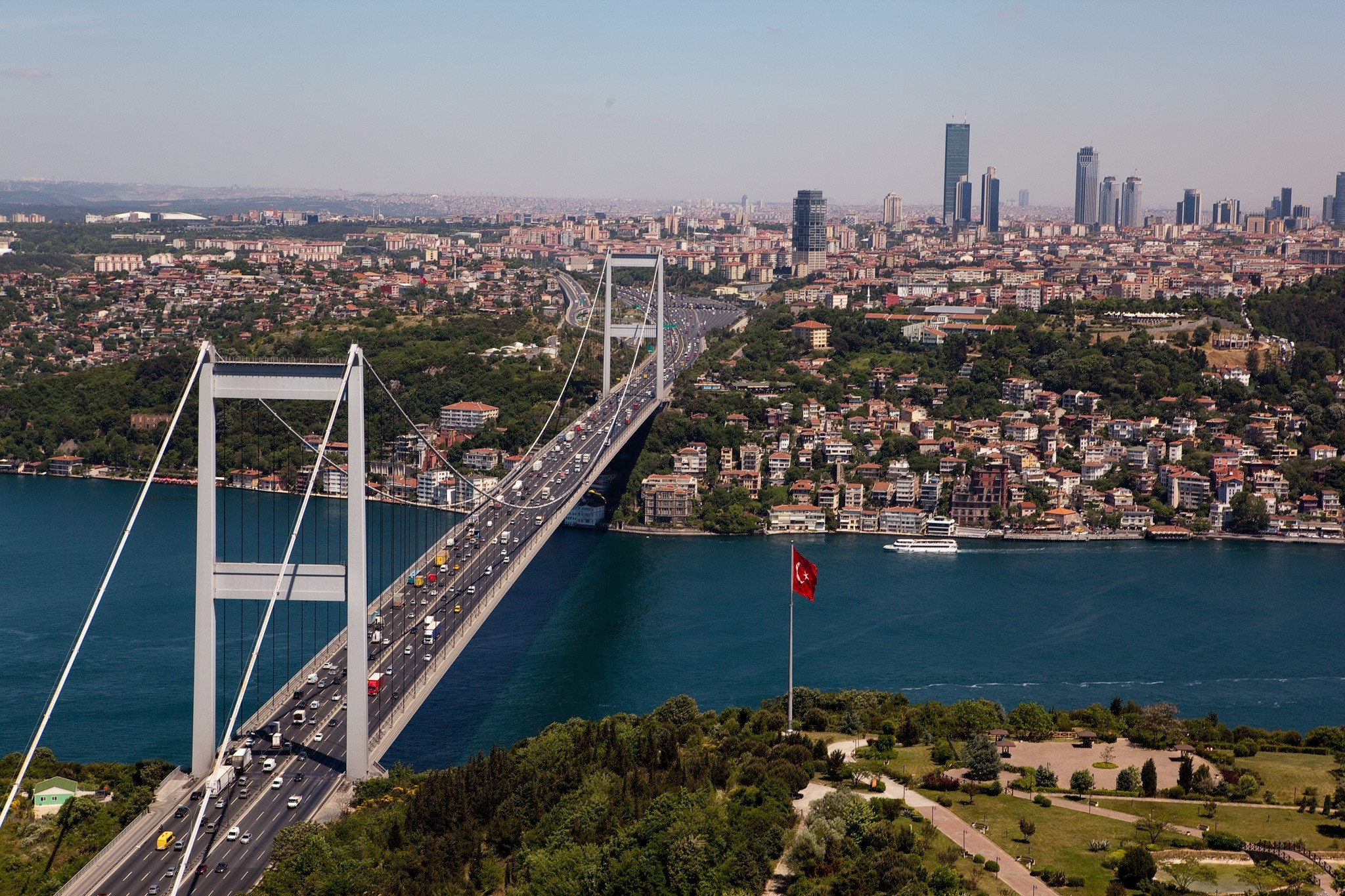 A panoramic view of Istanbul, showcasing the Fatih Sultan Mehmet Bridge spanning the Bosphorus Strait, with urban landscapes and lush greenery