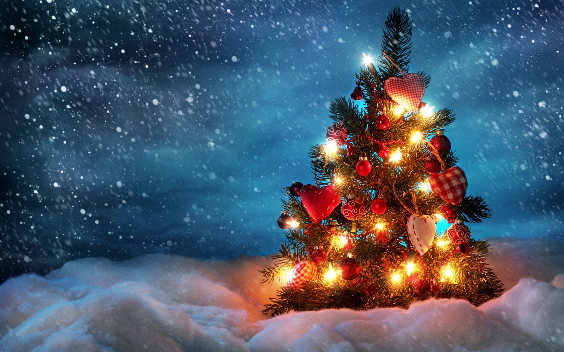 A Christmas tree decorated with lights and heart-shaped ornaments stands in a snowy landscape under a dark, snowy sky