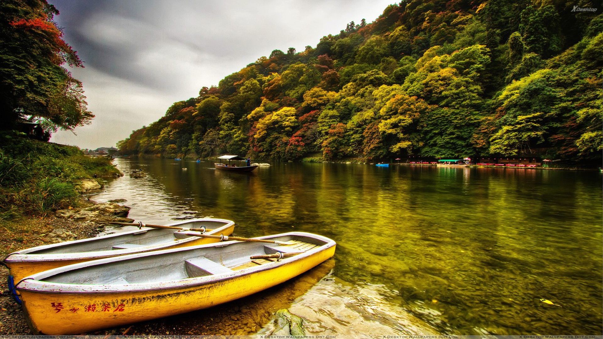 Two yellow rowboats rest on the shore of a tranquil river, surrounded by vibrant autumn foliage on the far bank. The serene scene captures the beauty of nature with a touch of tranquility