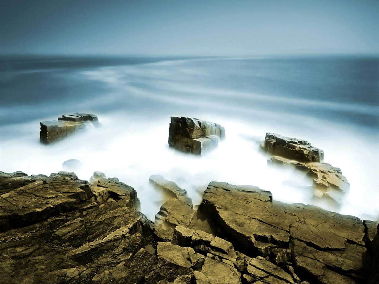 Long exposure photograph of rocks in the ocean with a misty, ethereal effect