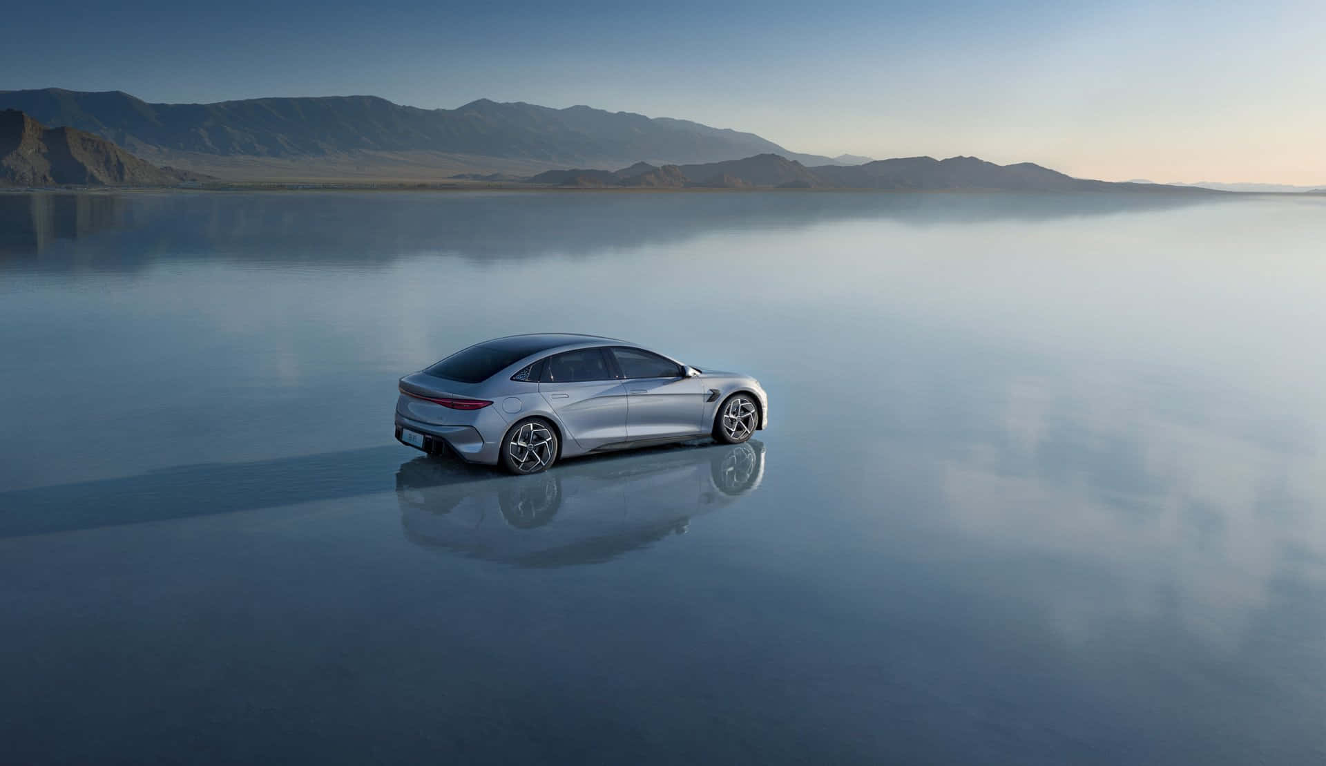 A silver BYD Seal electric sedan parked on a reflective surface with mountains in the background, showcasing its sleek design
