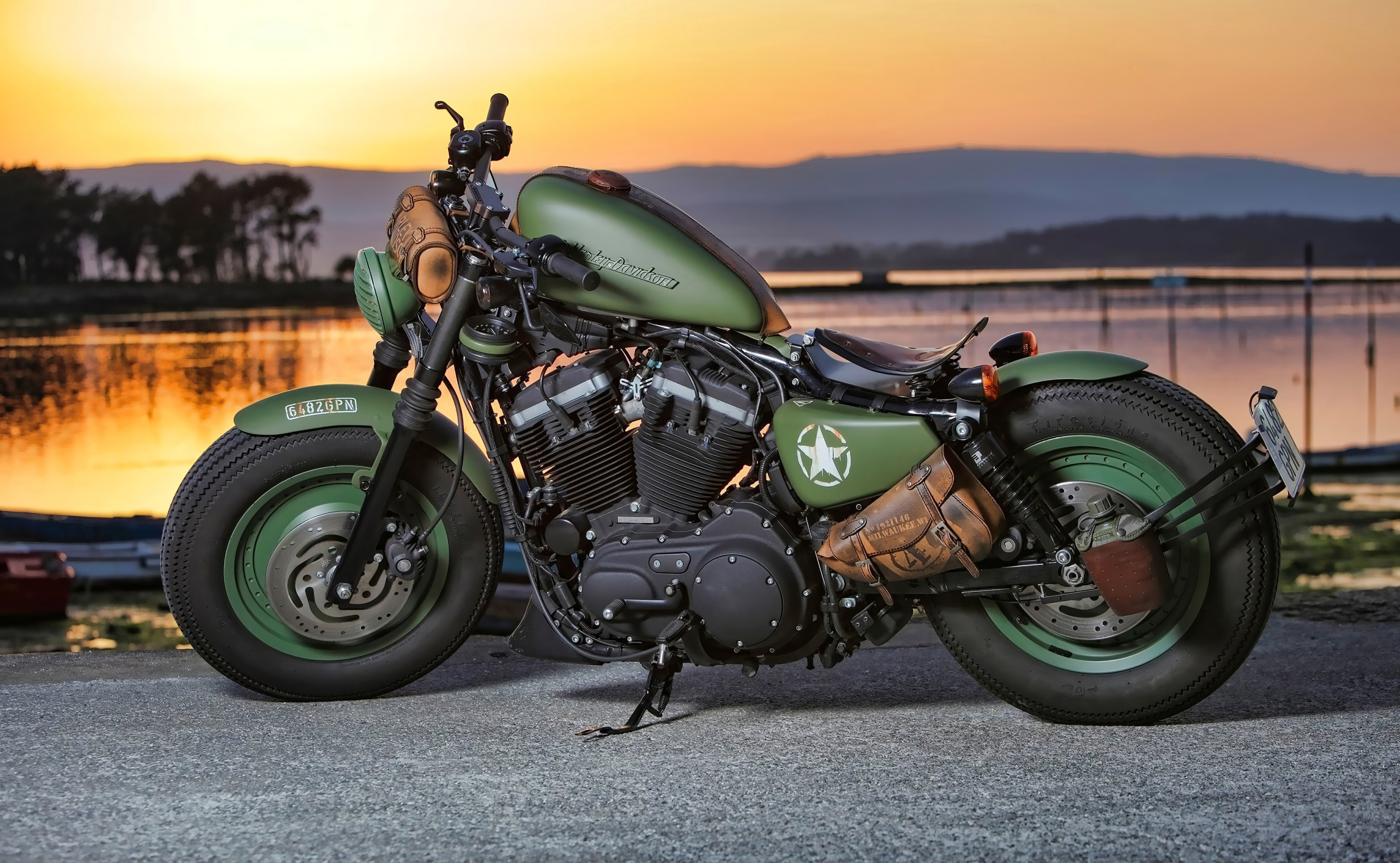Custom olive green Harley-Davidson motorcycle parked by a tranquil waterfront at sunset