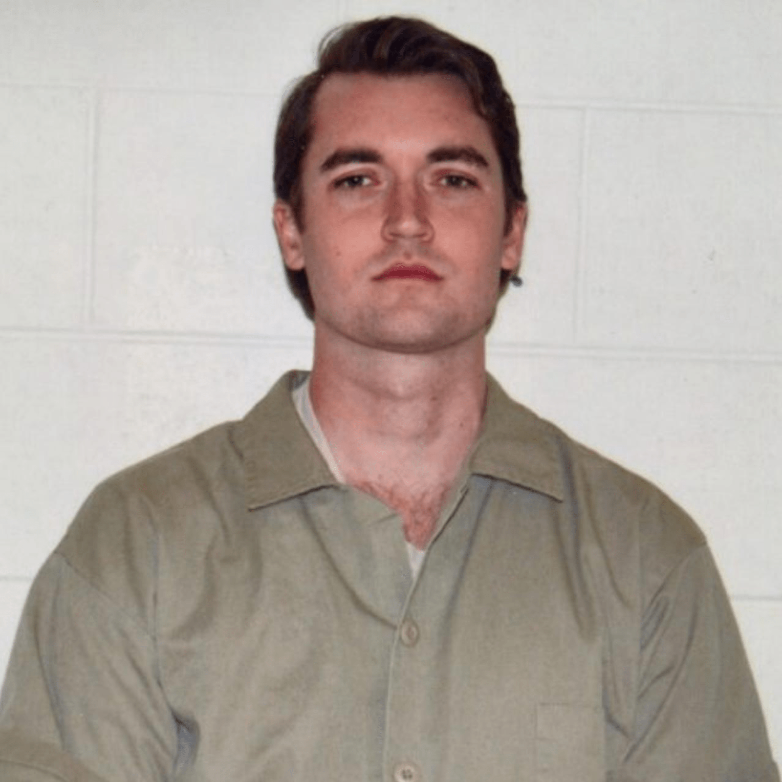 Ross Ulbricht in a mugshot, wearing a light olive green prison uniform. His expression is neutral, and his hair is neatly styled