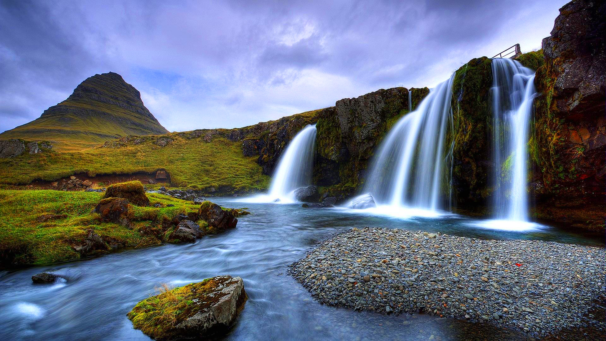 A stunning 4K landscape wallpaper featuring a cascading waterfall, a tranquil river, and a majestic mountain in the backdrop