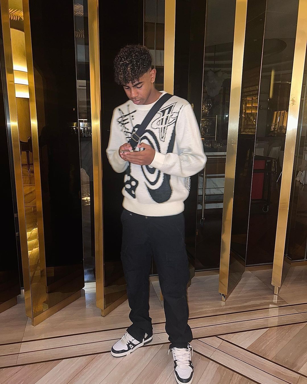 Lamine Yamal in a stylish outfit, looking at his phone