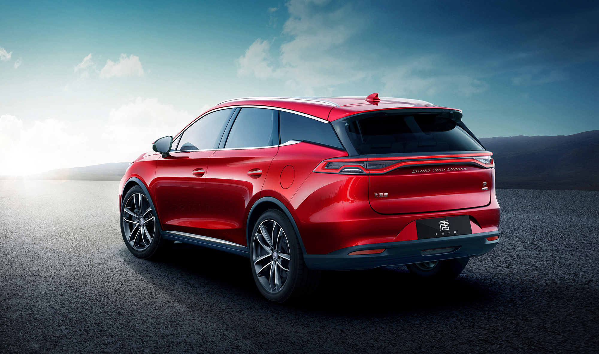 A rear view of a red BYD Song L, parked on a paved road against a mountainous backdrop under a clear sky