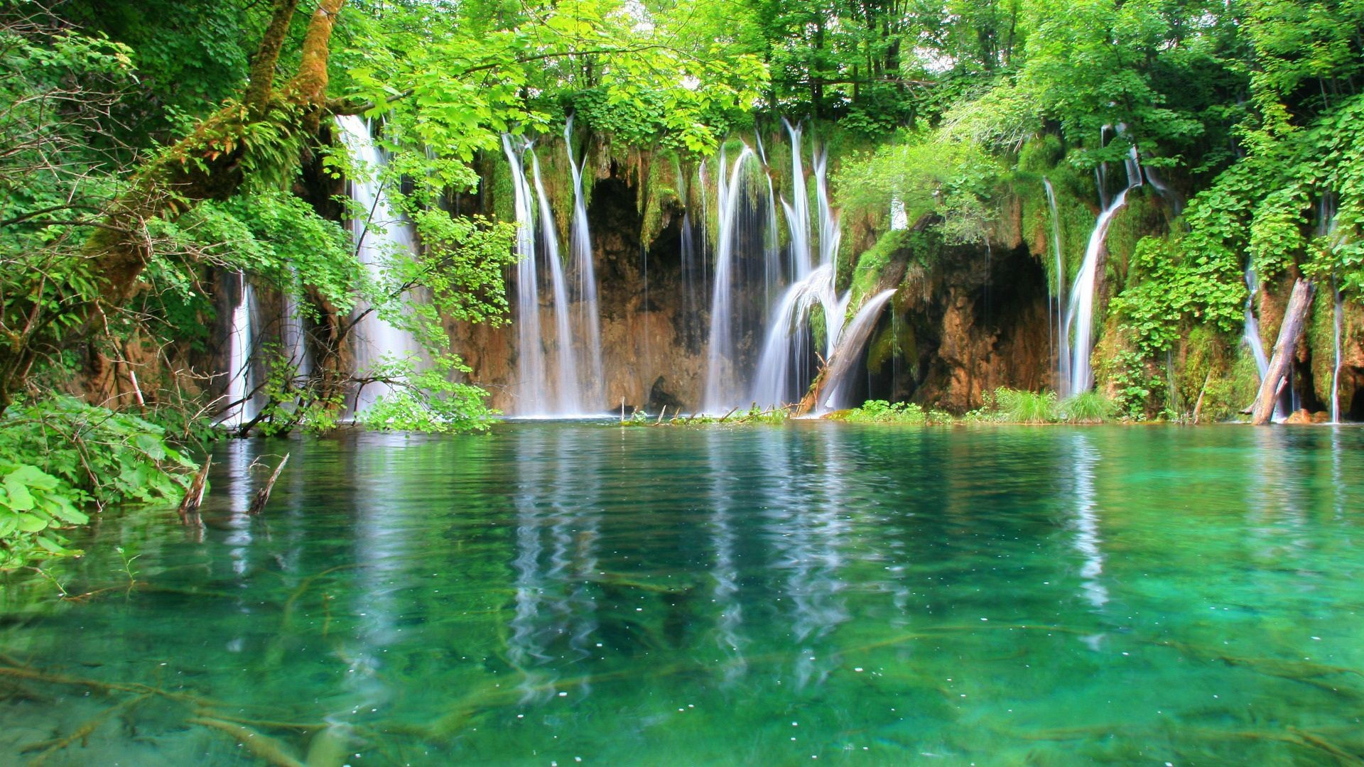 Scenic waterfall cascading into a crystal-clear turquoise pool in a lush green forest, ideal for a desktop background