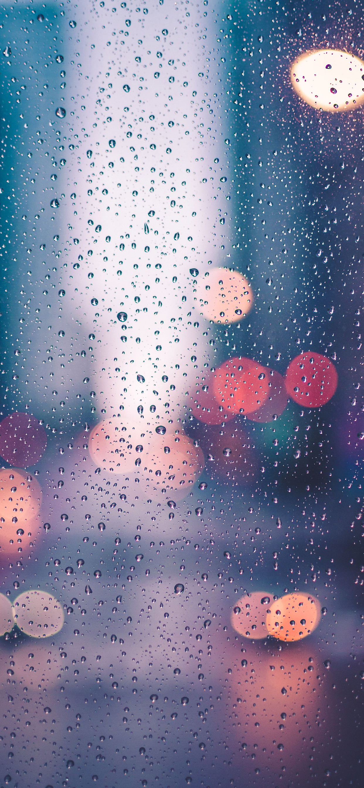 Close-up of raindrops on a window with blurred city lights in the background