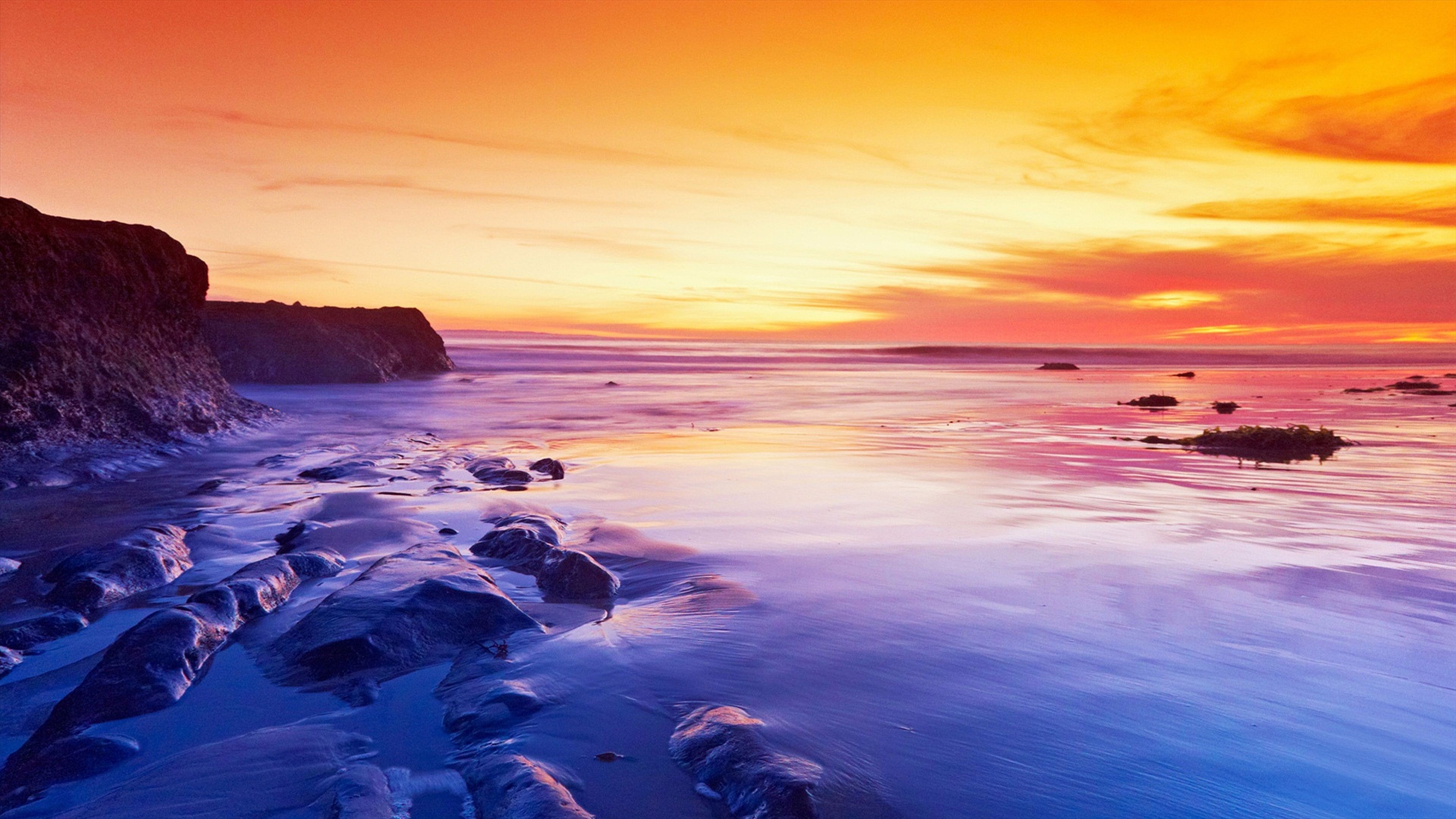 Vivid sunset over a rocky beach, creating a vibrant and colorful wallpaper