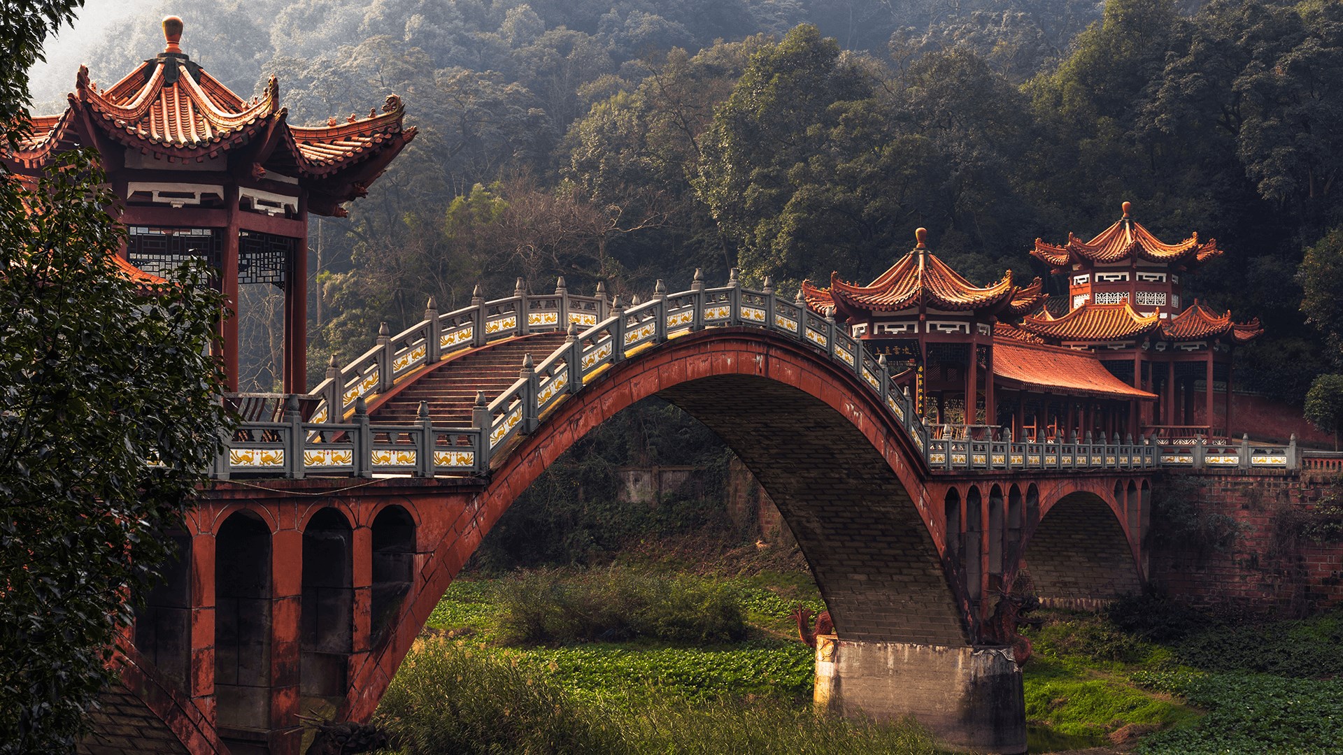 A picturesque arched bridge in a traditional Chinese style, connecting two ornate pavilions amidst a lush green landscape