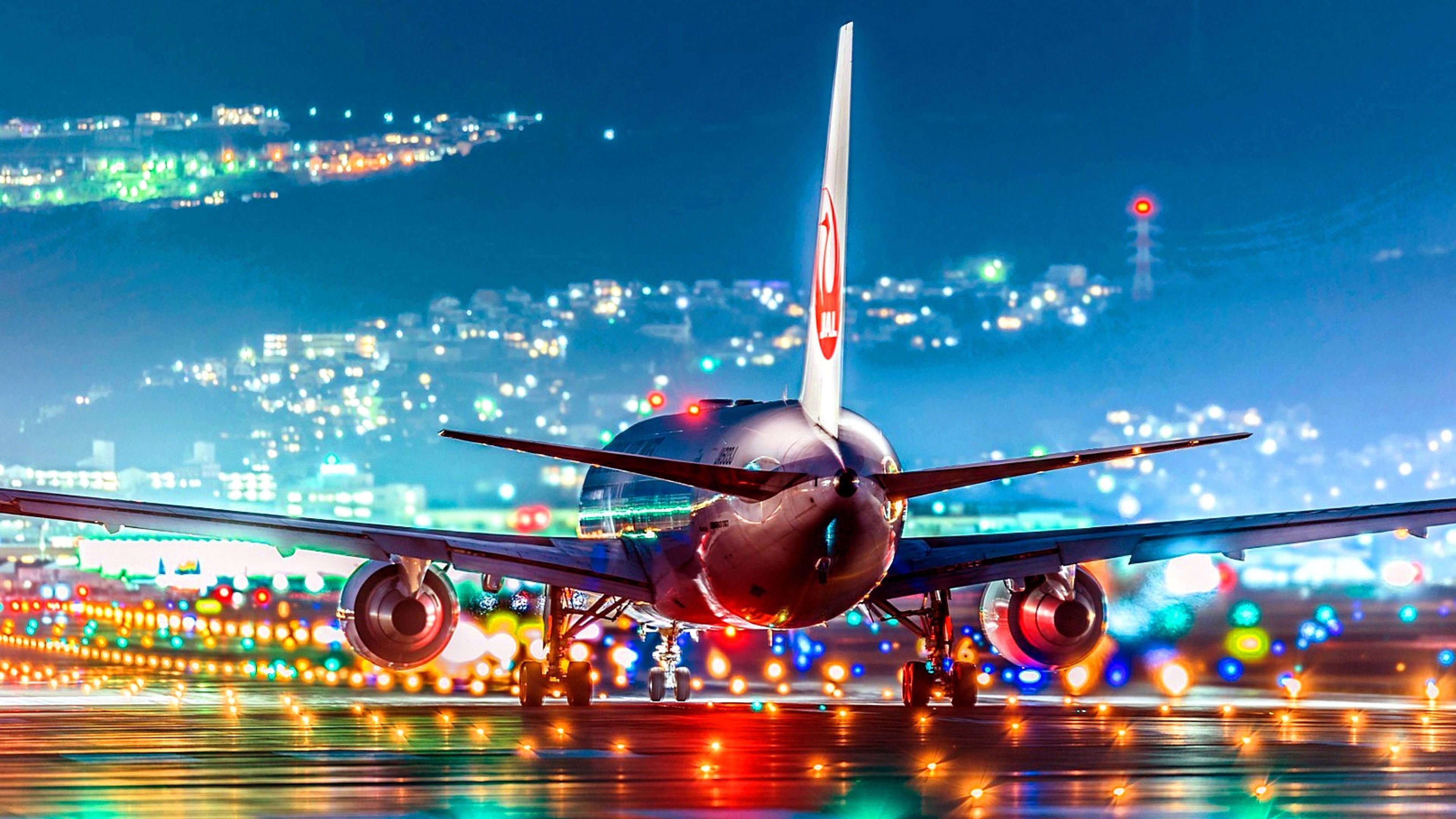 A Japan Airlines 777 airplane on the runway at night, with city lights in the background