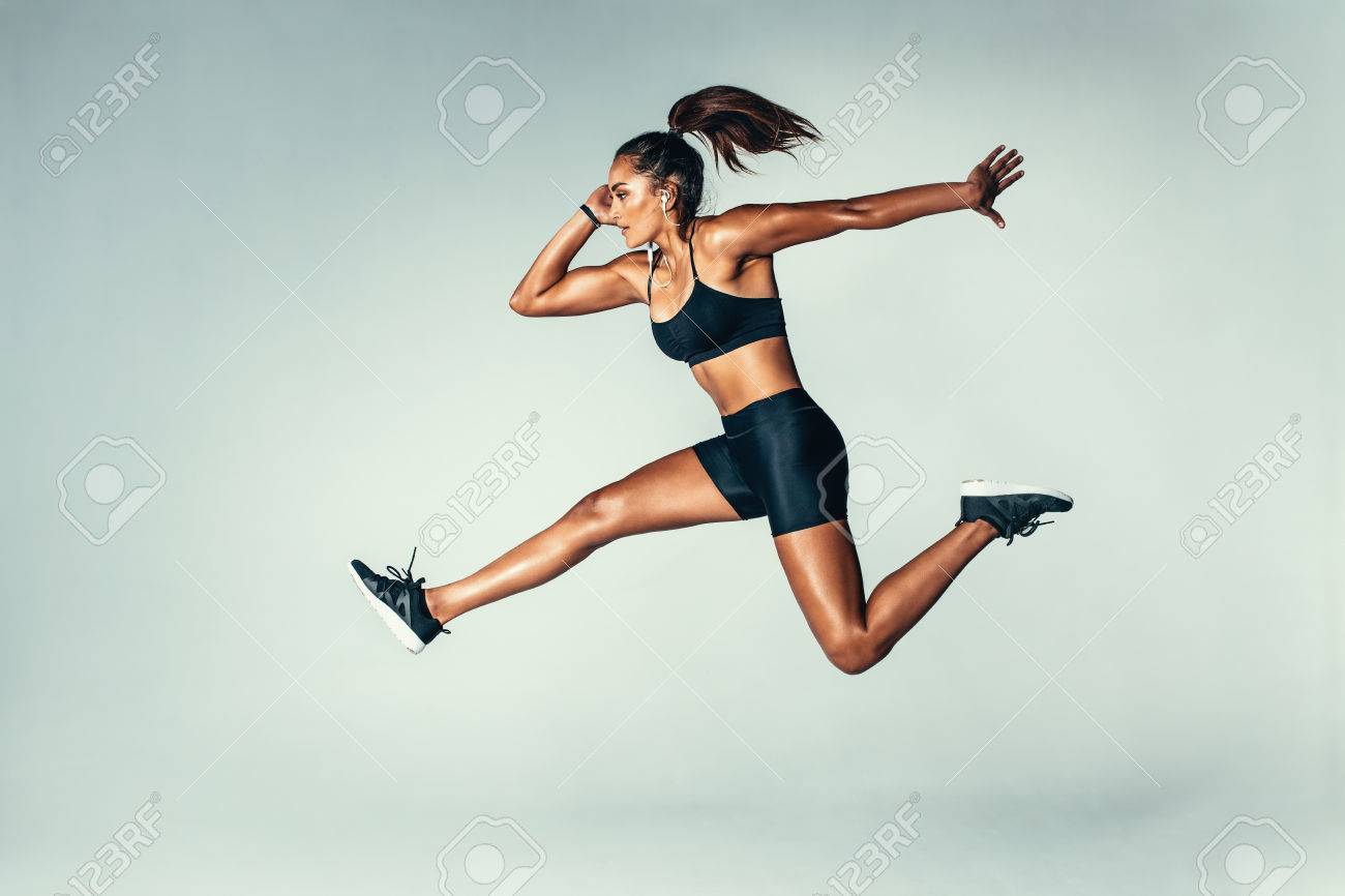 Side Of Fit Young Woman Jumping Against Grey Background