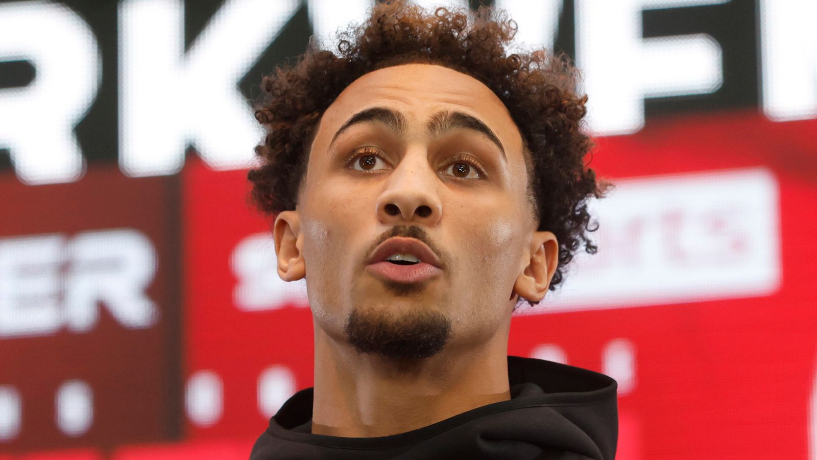 Benjamin Whittaker at a press conference, looking upwards with a thoughtful expression