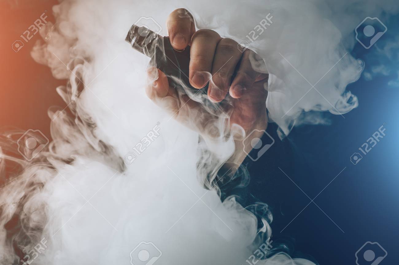 Man Hand Shows Vape Device At Cloud Of Vapor Background