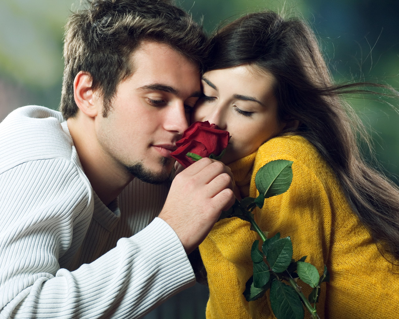 A young couple shares a romantic moment, smelling a red rose together