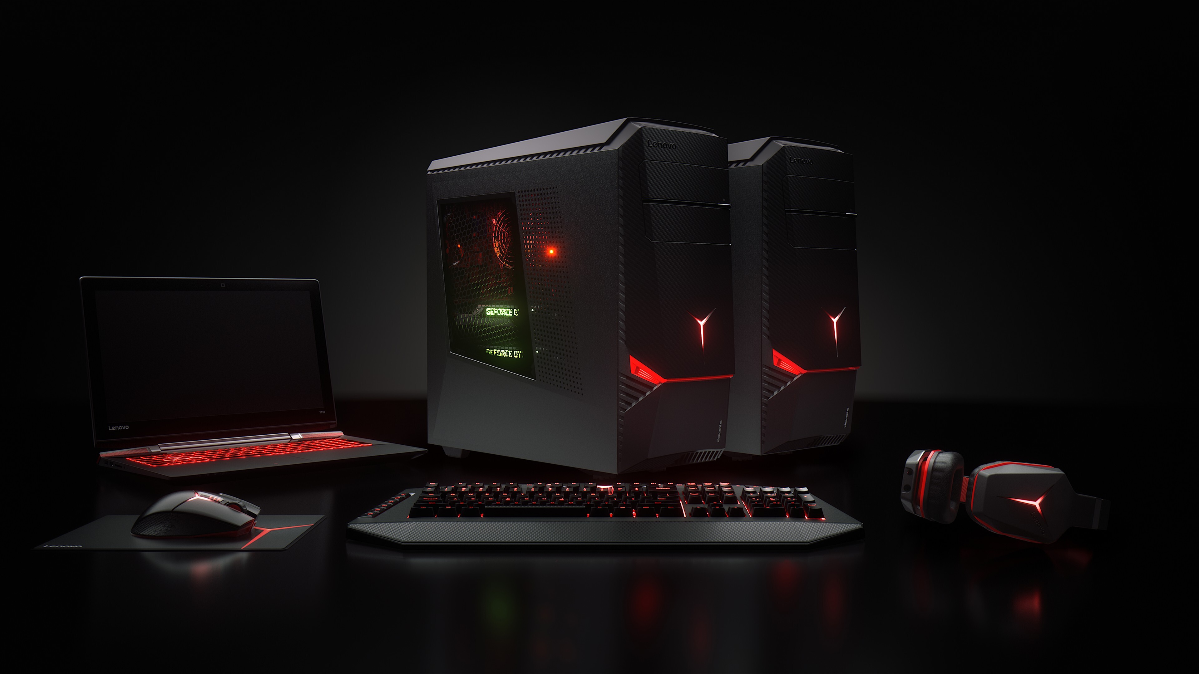 High-end Lenovo gaming setup with desktop PCs, laptop, keyboard, mouse, and headset, illuminated with red accents against a dark background