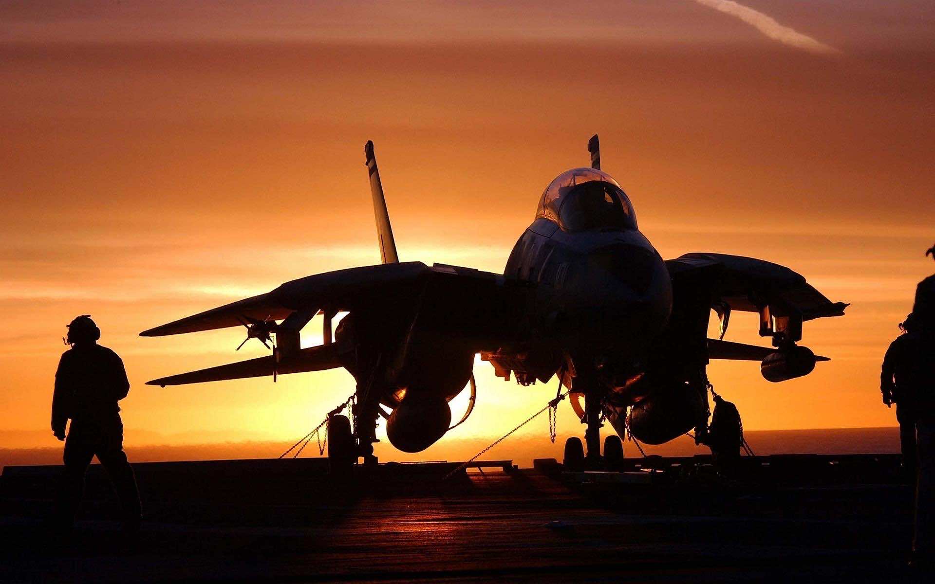Silhouette of a fighter jet on an aircraft carrier deck during sunset