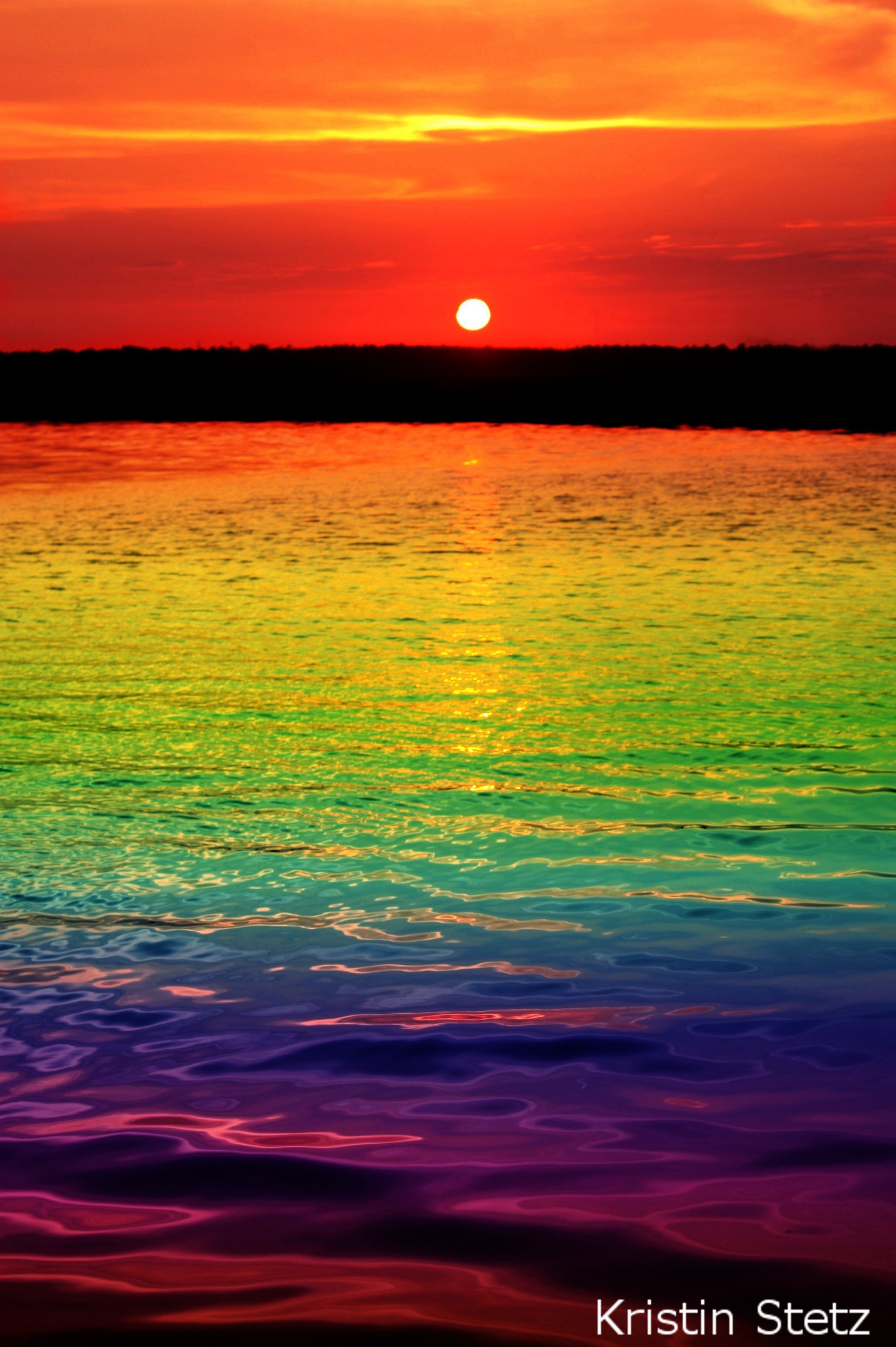 Vivid rainbow sunset over a tranquil body of water
