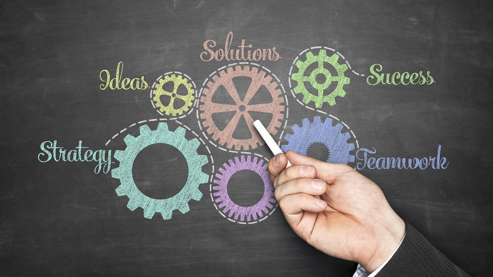Chalkboard drawing of interconnected gears representing business concepts like strategy, ideas, solutions, teamwork, and success