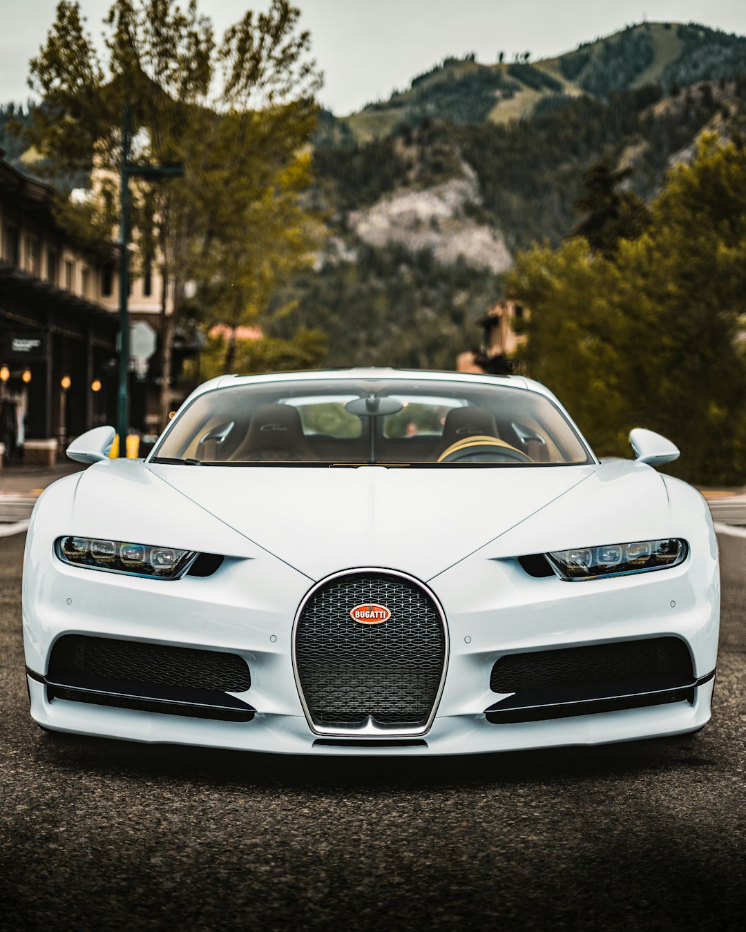 A white Bugatti Chiron sports car parked on a street with a mountain backdrop