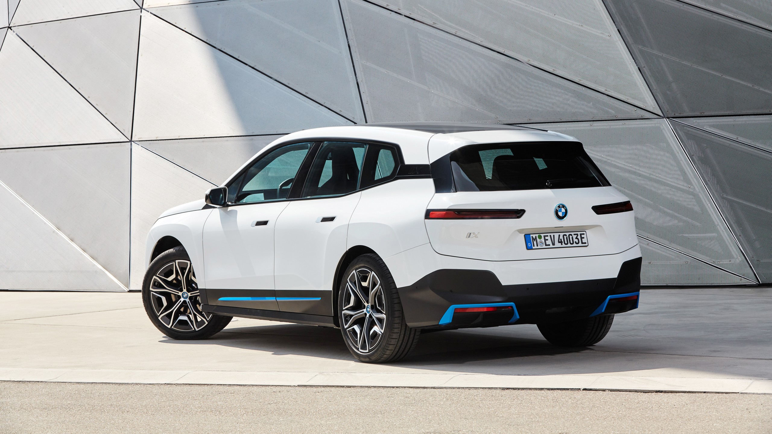 A rear view of a white BMW iX electric SUV parked in front of a modern architectural structure