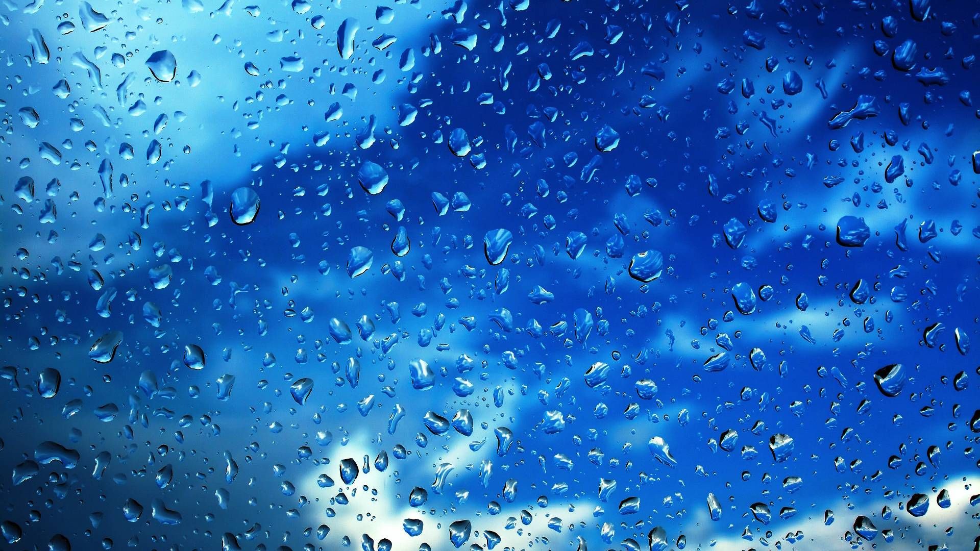 Close-up of raindrops on a window against a blue sky with clouds