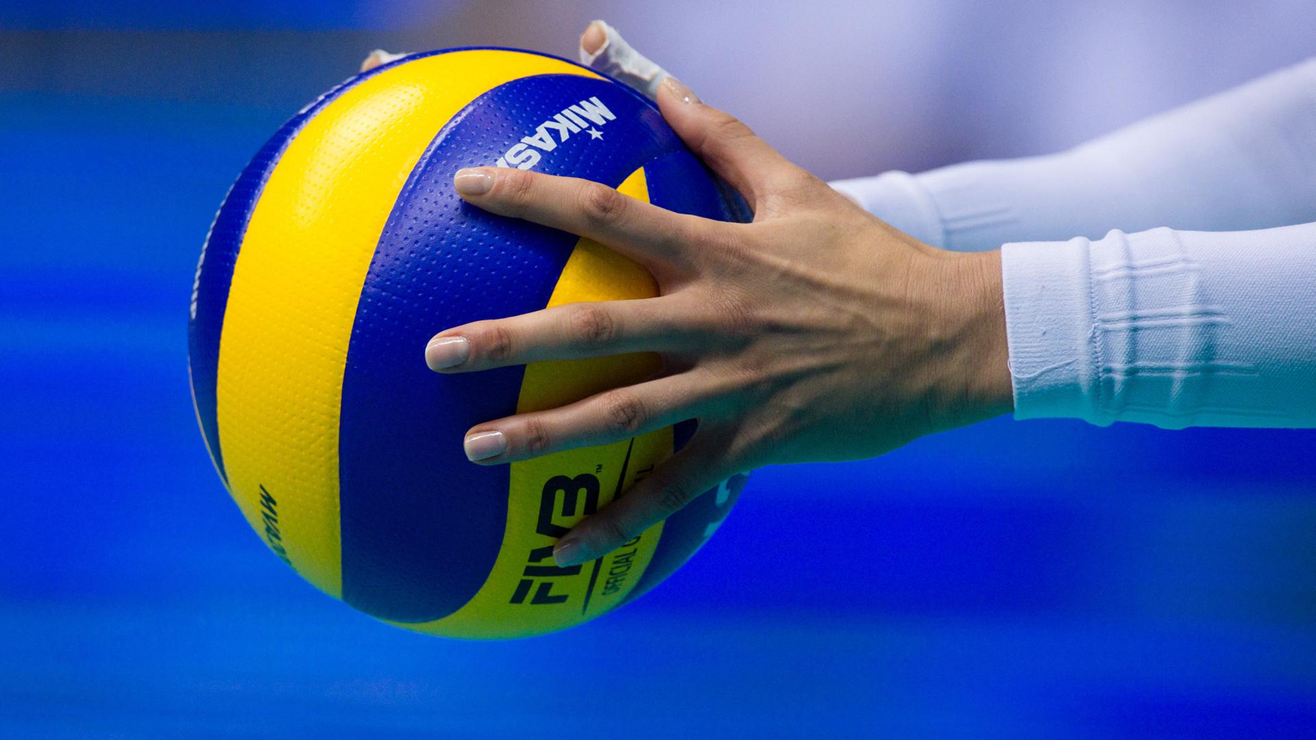 Close-up of hands holding a volleyball against a blue background