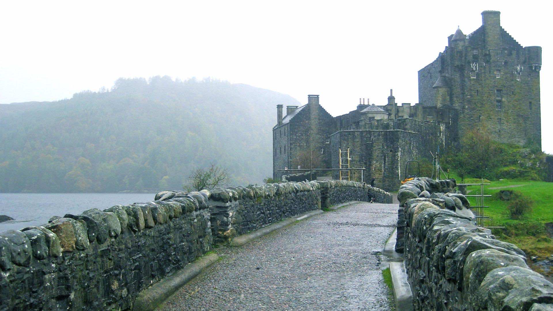 A stone bridge leading to a historic castle on a rainy day
