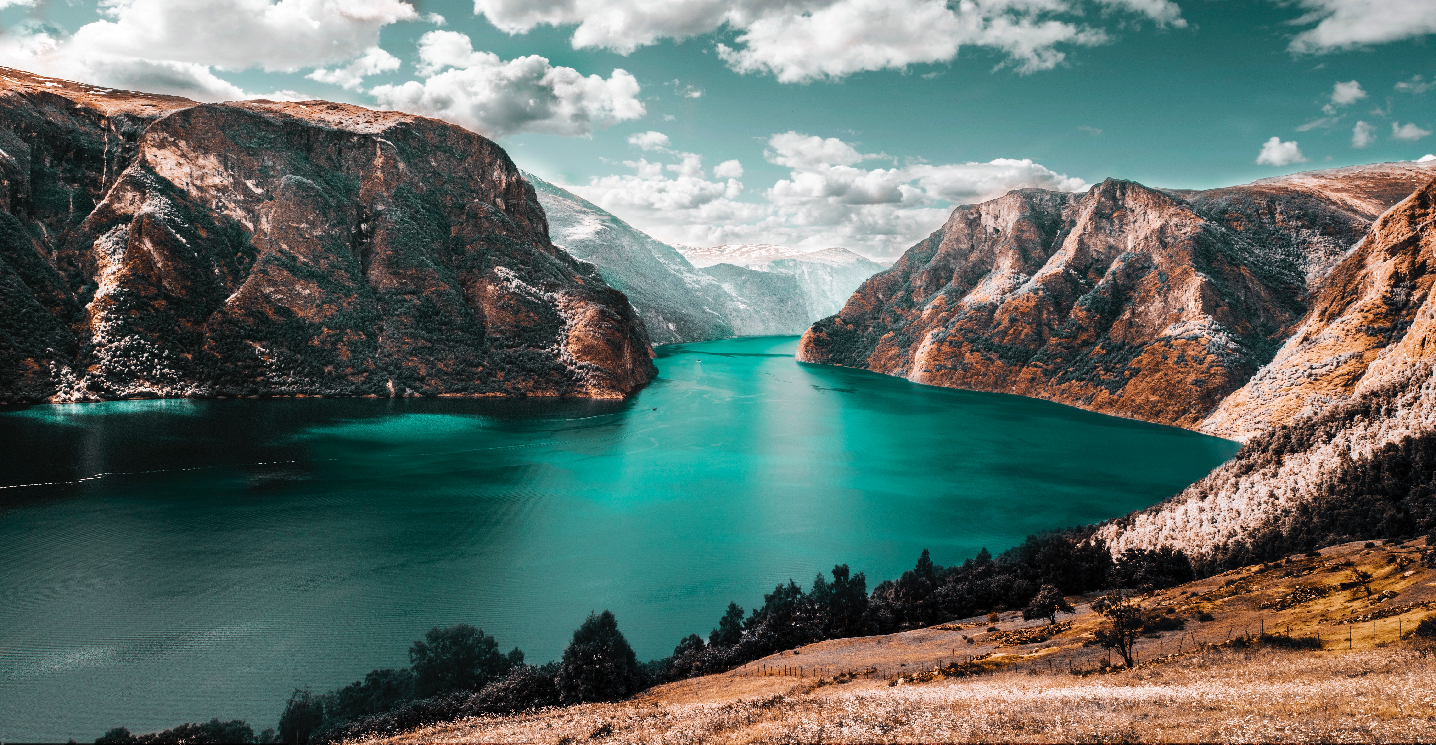 Stunning 4K background image of a turquoise fjord nestled between rugged, colorful mountains under a dramatic sky