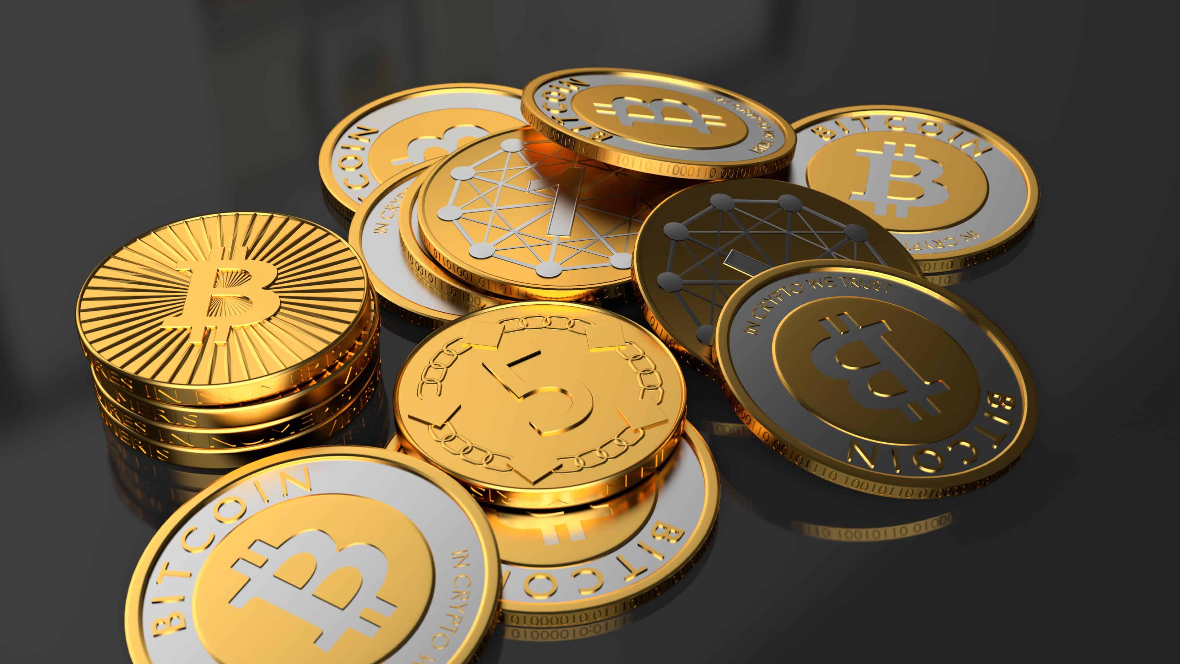 A close-up view of various gold and silver cryptocurrency coins, including Bitcoin, scattered on a dark reflective surface