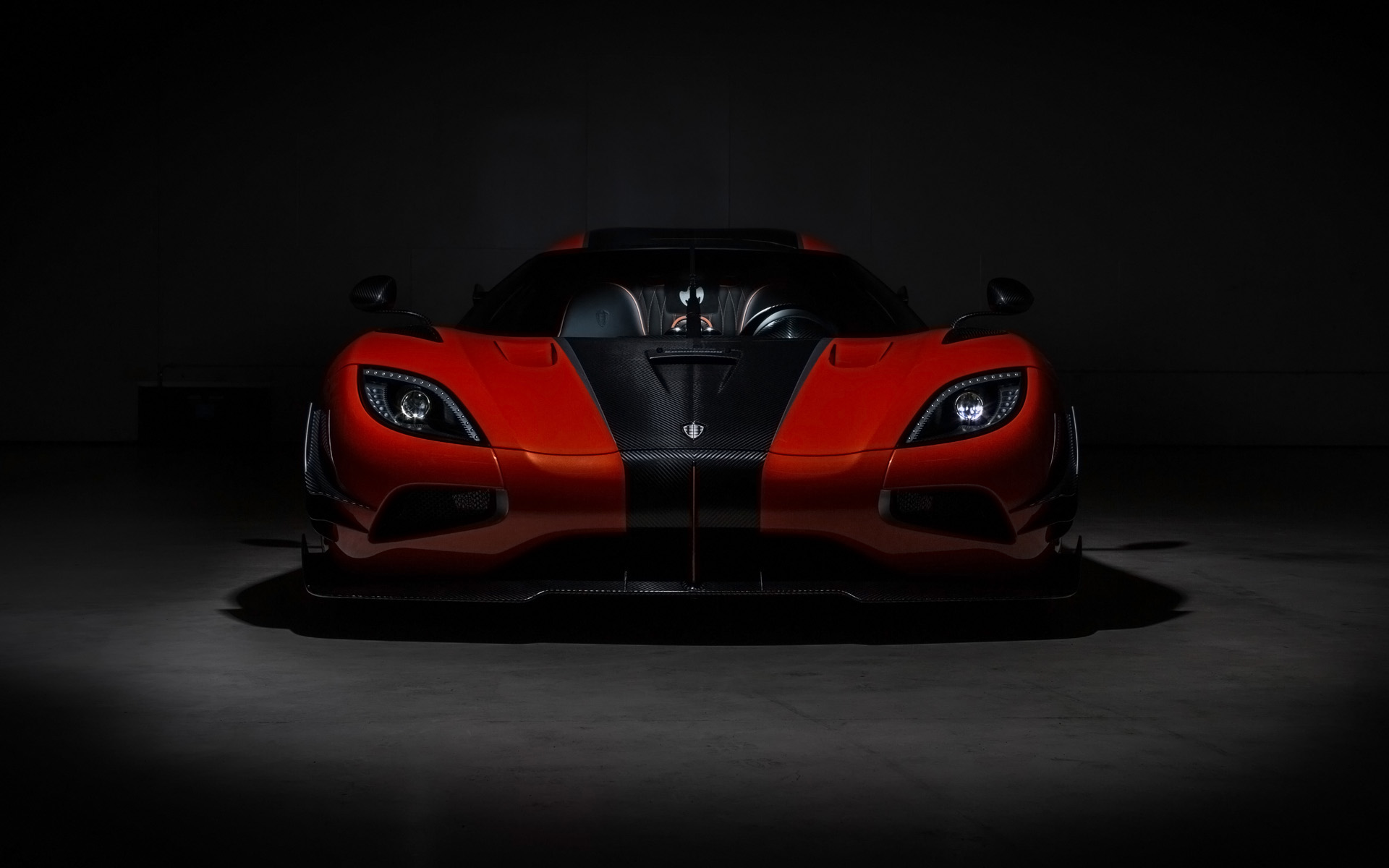 A front view of a sleek, red and black Koenigsegg Agera sports car in a dark setting, highlighting its aggressive design and carbon fiber accents