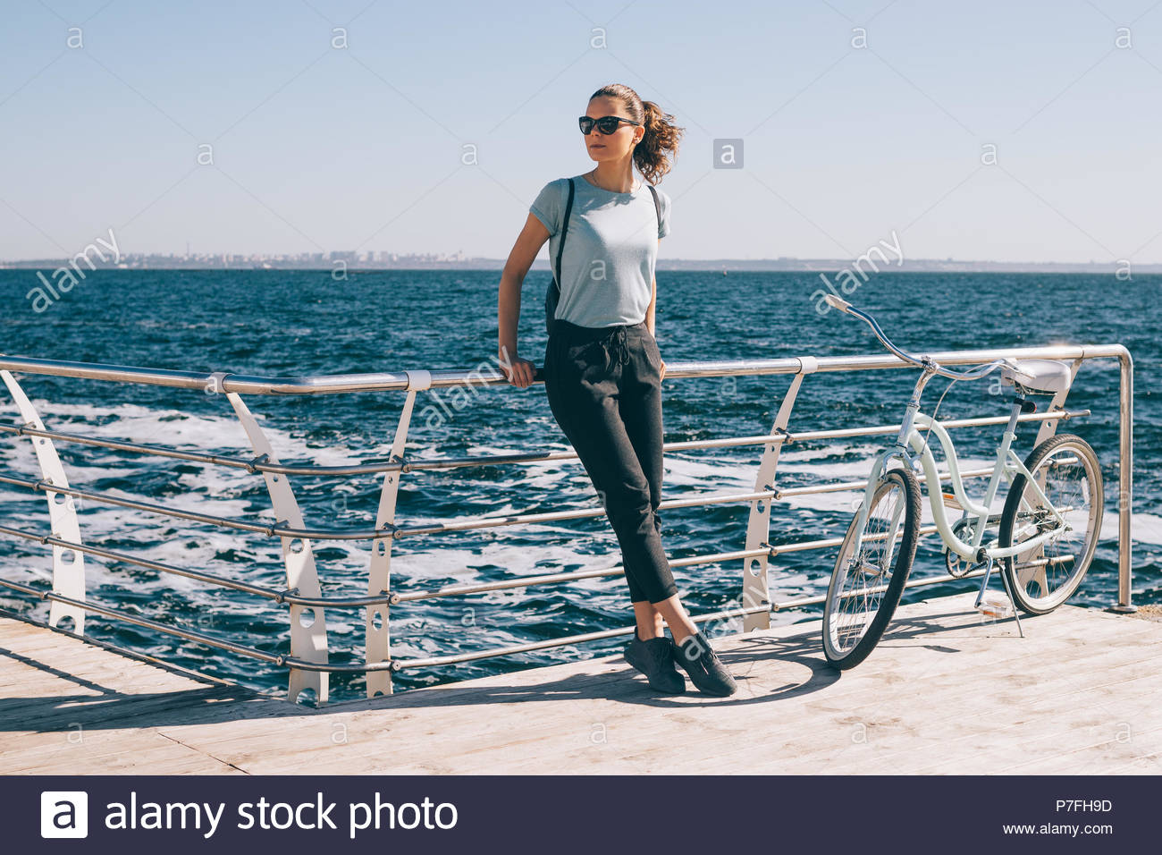 Slender Young Woman Standing At The Background Of Blue Sea Near