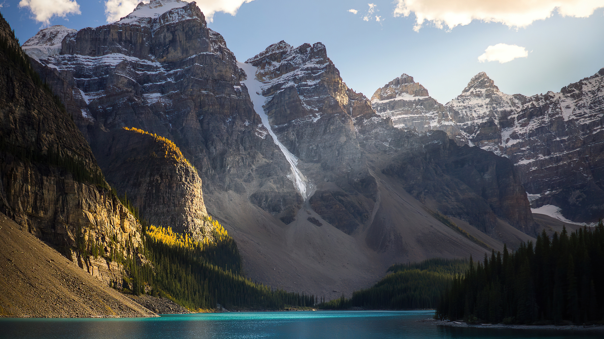 Moraine Lake in Banff National Park, showcasing its vibrant turquoise waters, dramatic snow-capped mountains, and lush evergreen forests under a partially cloudy sky, reflecting the iconic Canadian Rockies scenery in stunning 4K resolution