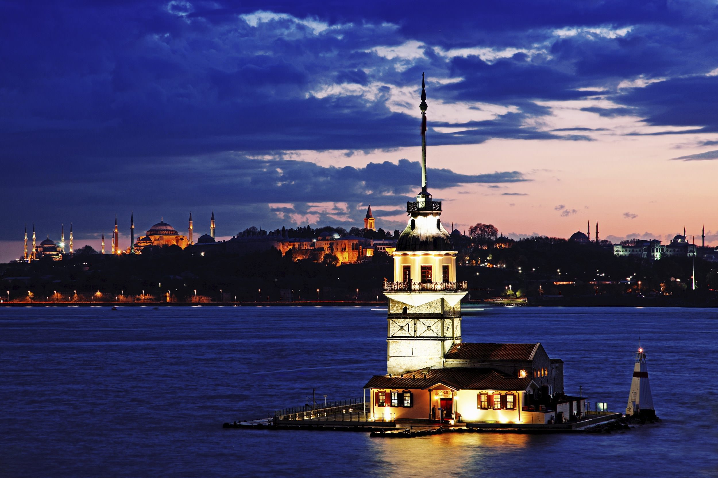 The Maiden's Tower, a historic landmark in Istanbul, stands illuminated against the backdrop of the Bosphorus and the city skyline at sunset