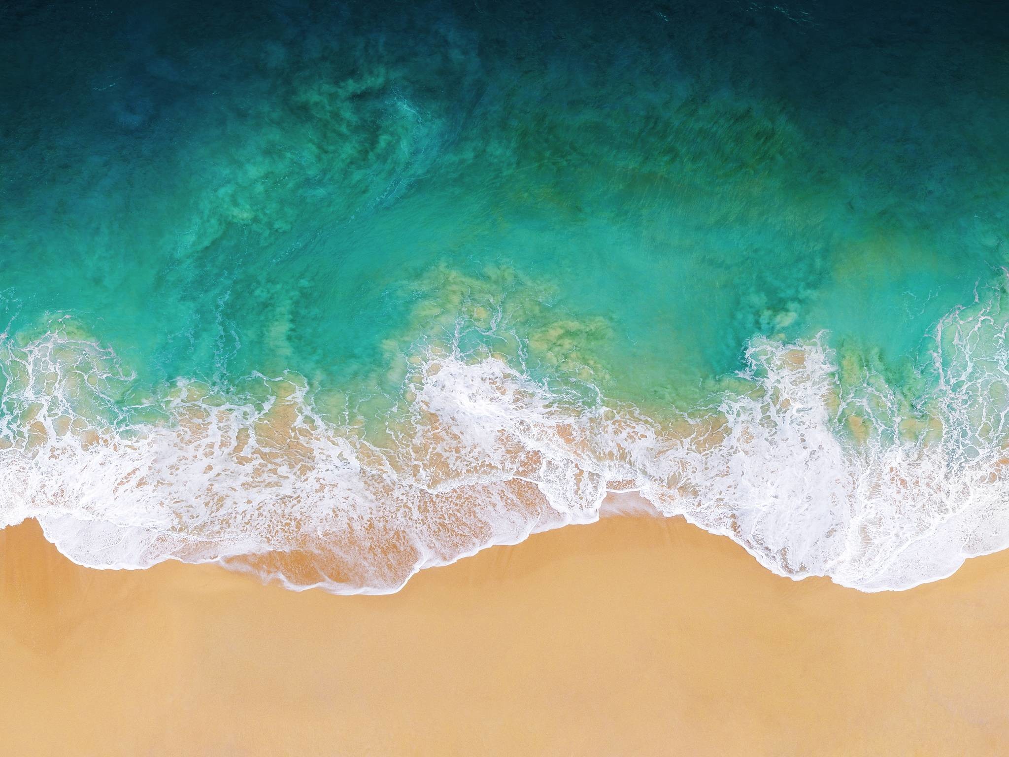 Aerial view of turquoise ocean waves crashing on a sandy beach, creating a stunning natural abstract