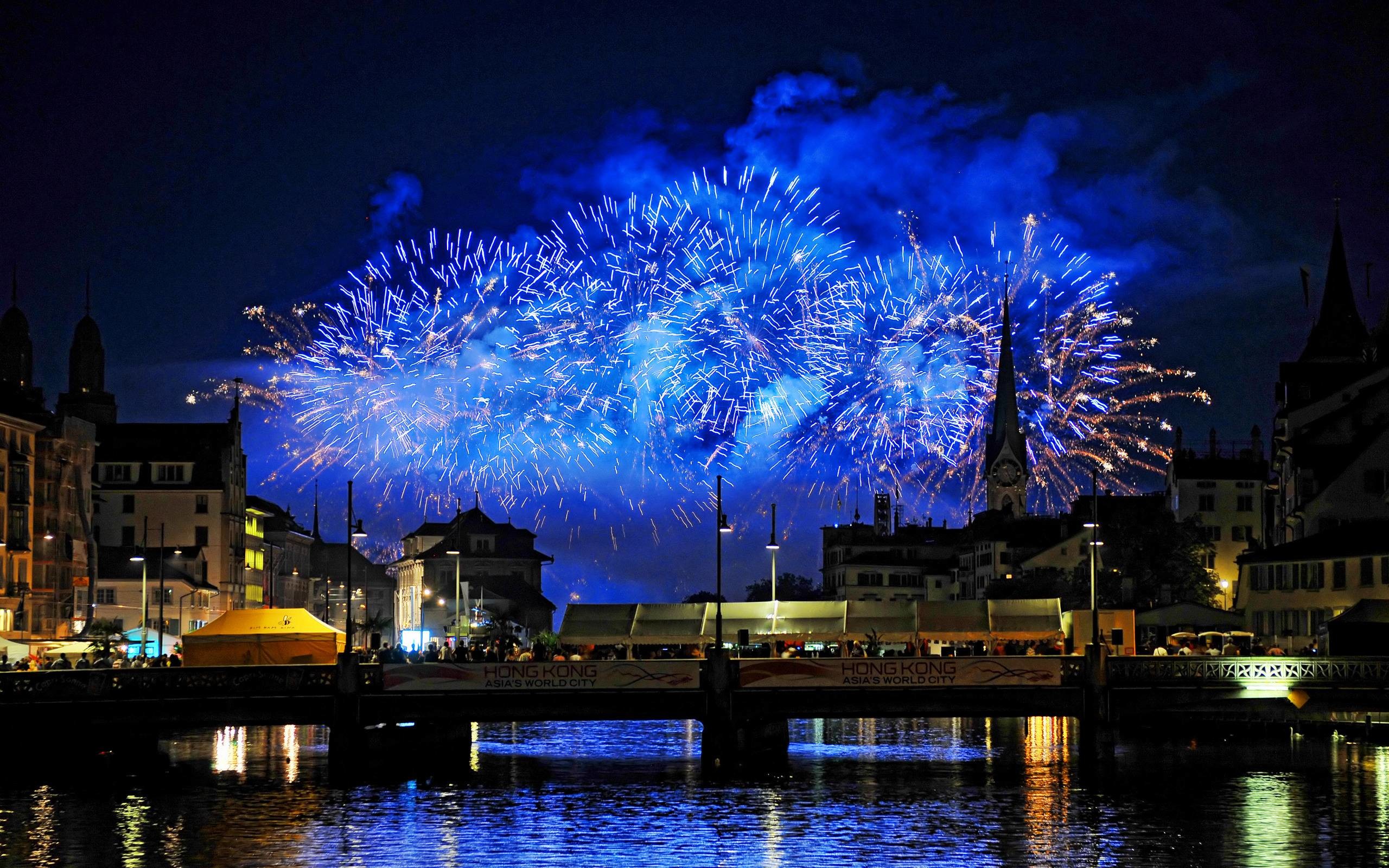 Fireworks light up the night sky over a city, reflecting in the water below, creating a festive New Year's scene