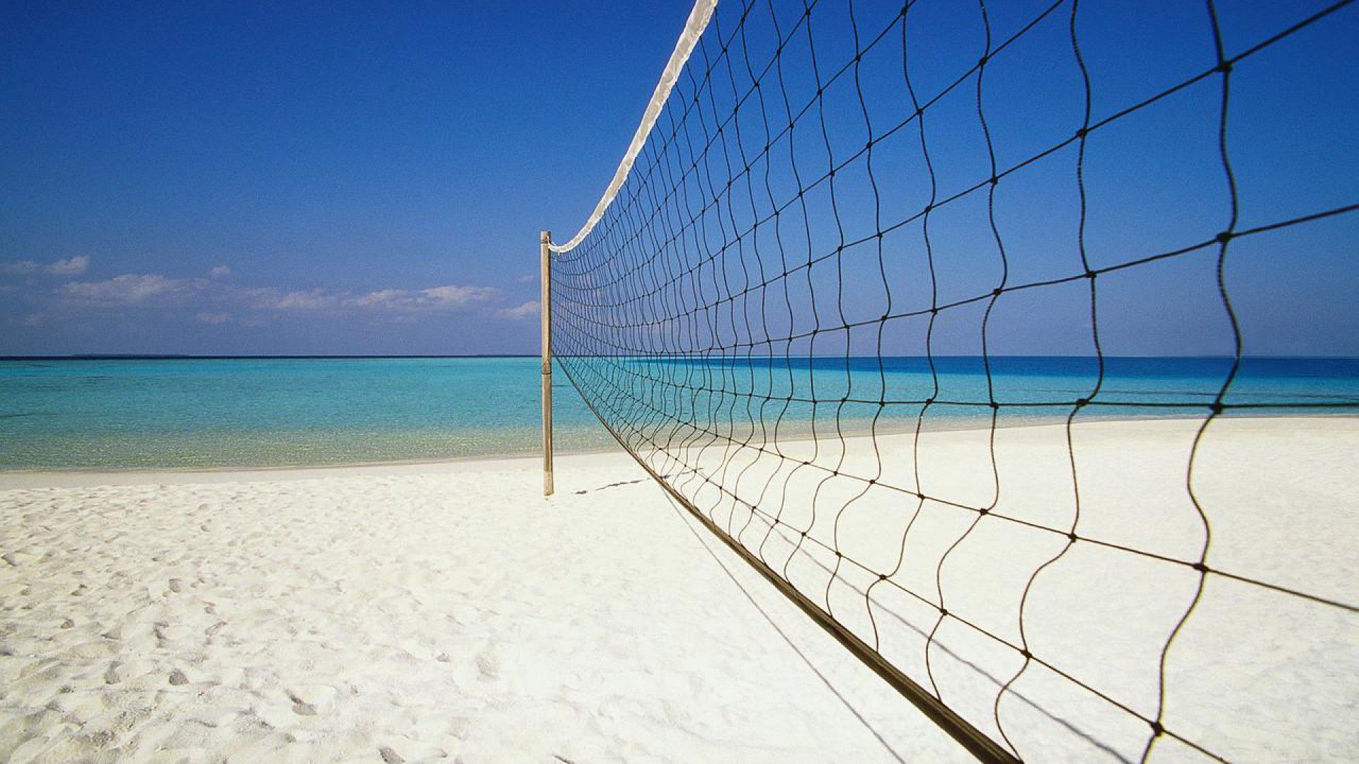 Beach volleyball net set up on a pristine white sand beach, with the turquoise ocean in the background