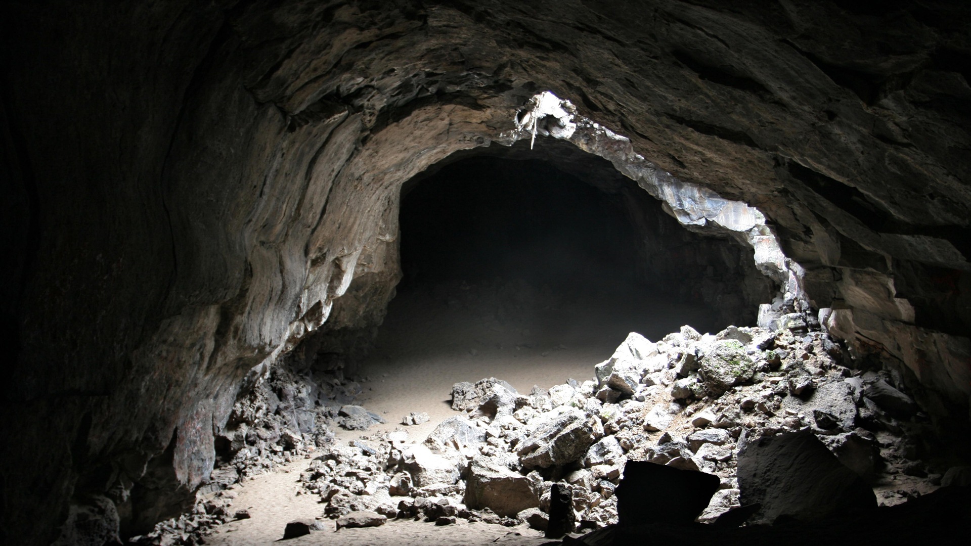 A dark and mysterious cave interior with a small opening letting in light, illuminating the rocky floor and walls
