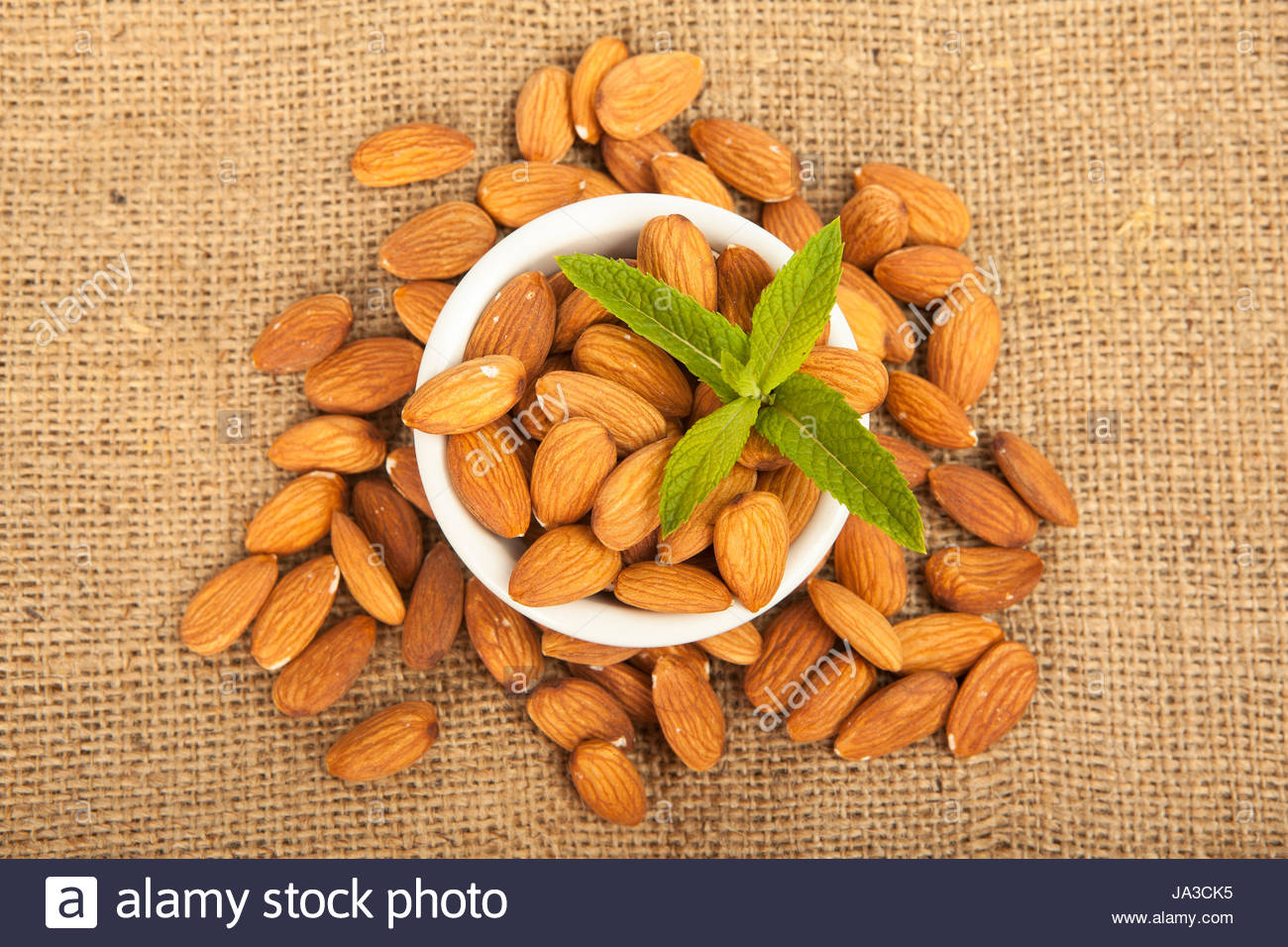 manu almonds in white ceramic bowl on sack background Stock Photo