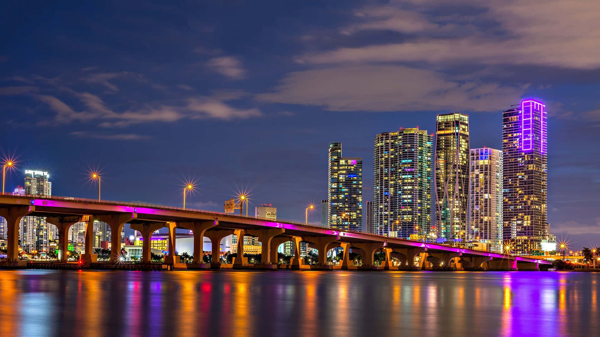 Vibrant Miami skyline at night with illuminated bridge and skyscrapers reflecting in the water