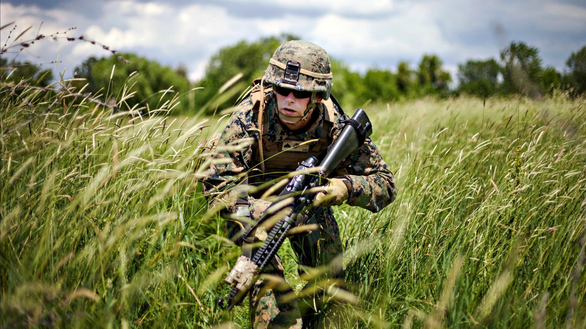 A soldier in camouflage uniform, helmet, and protective eyewear, stealthily advances through tall grass, gripping his rifle, embodying the intensity and focus of military operations
