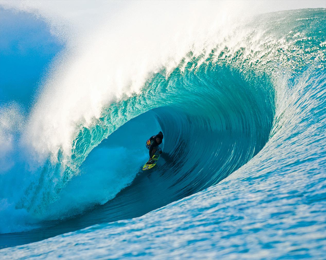 A surfer rides a massive, turquoise blue wave in a surfing competition, showcasing the power and beauty of the ocean