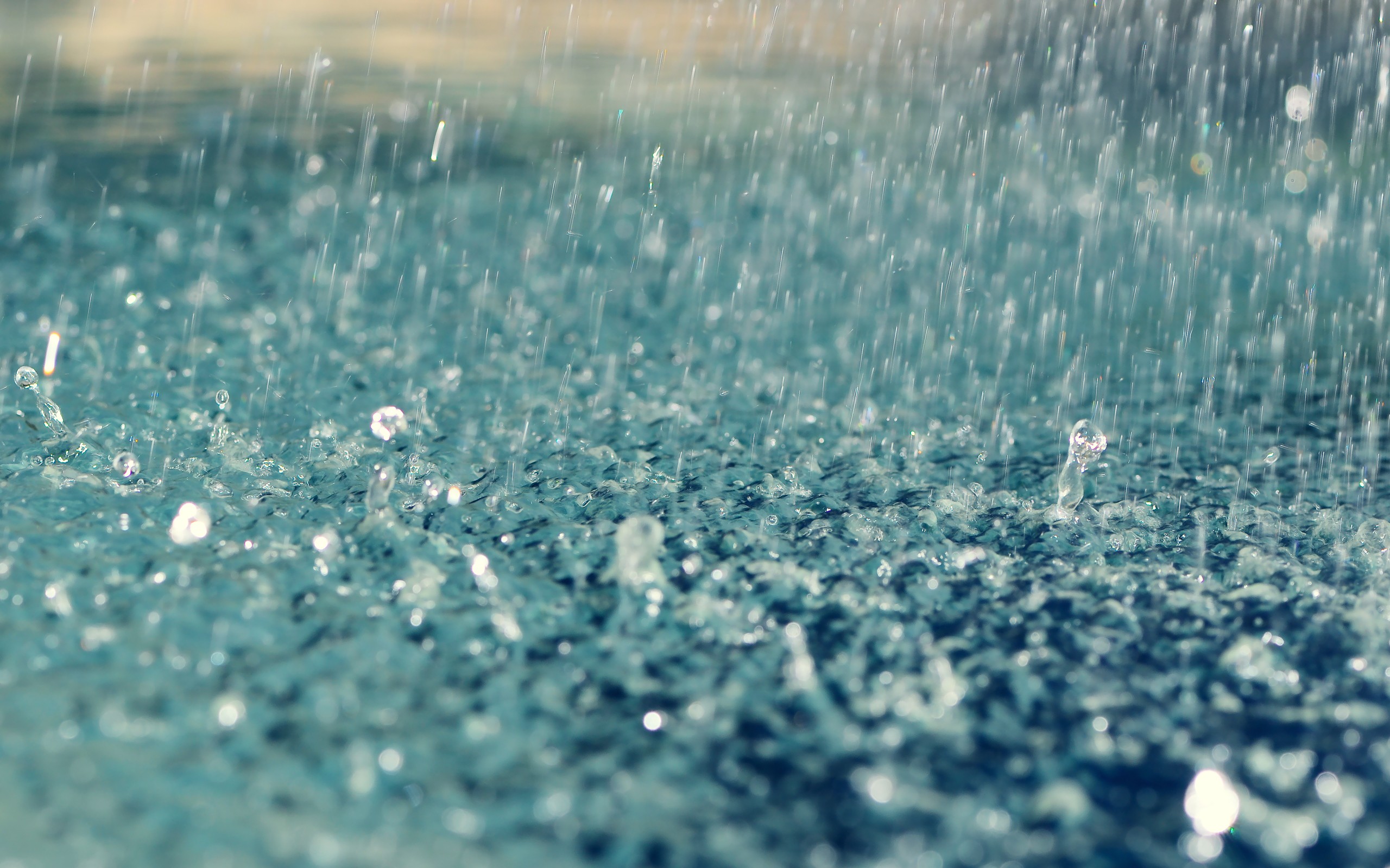Close-up of raindrops splashing into a pool of water, creating ripples and textures