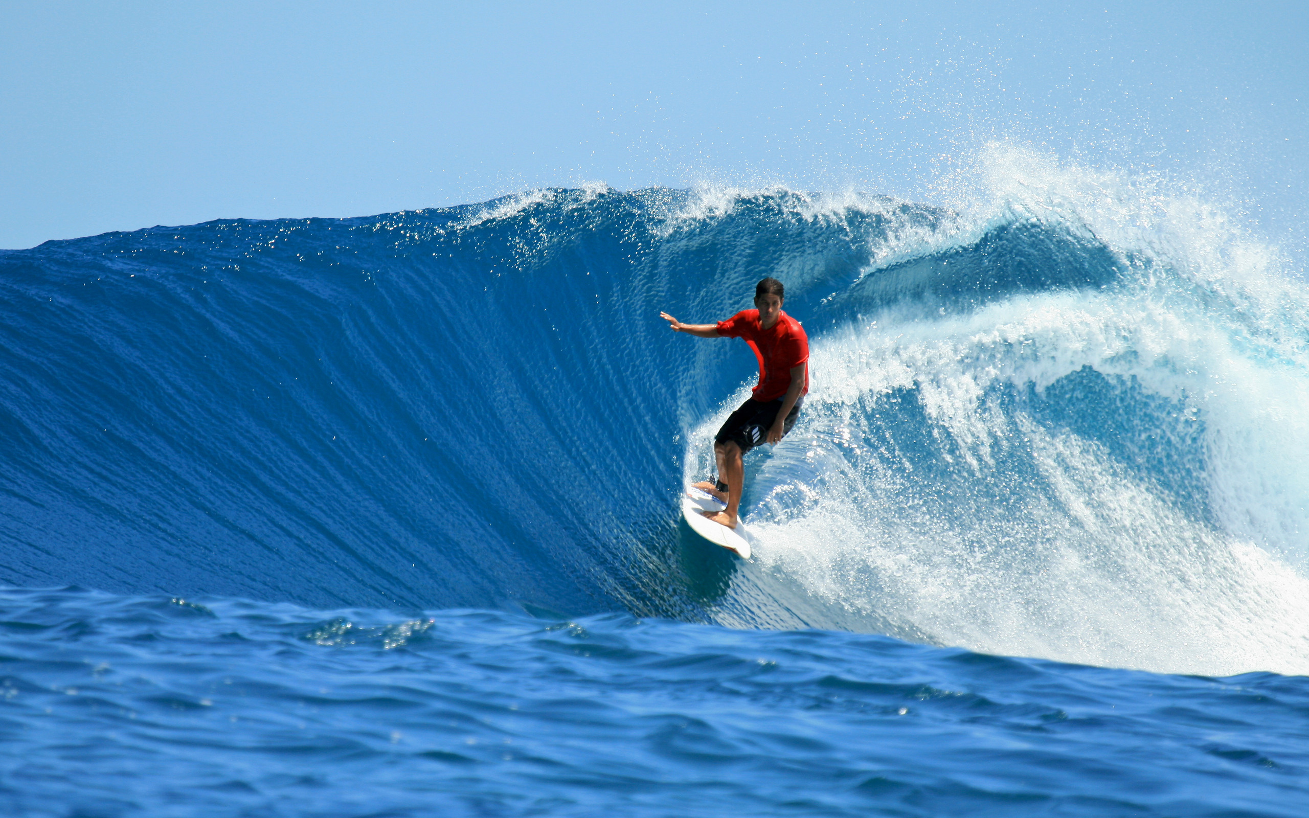A surfer in a red rash guard rides a powerful blue wave in the ocean