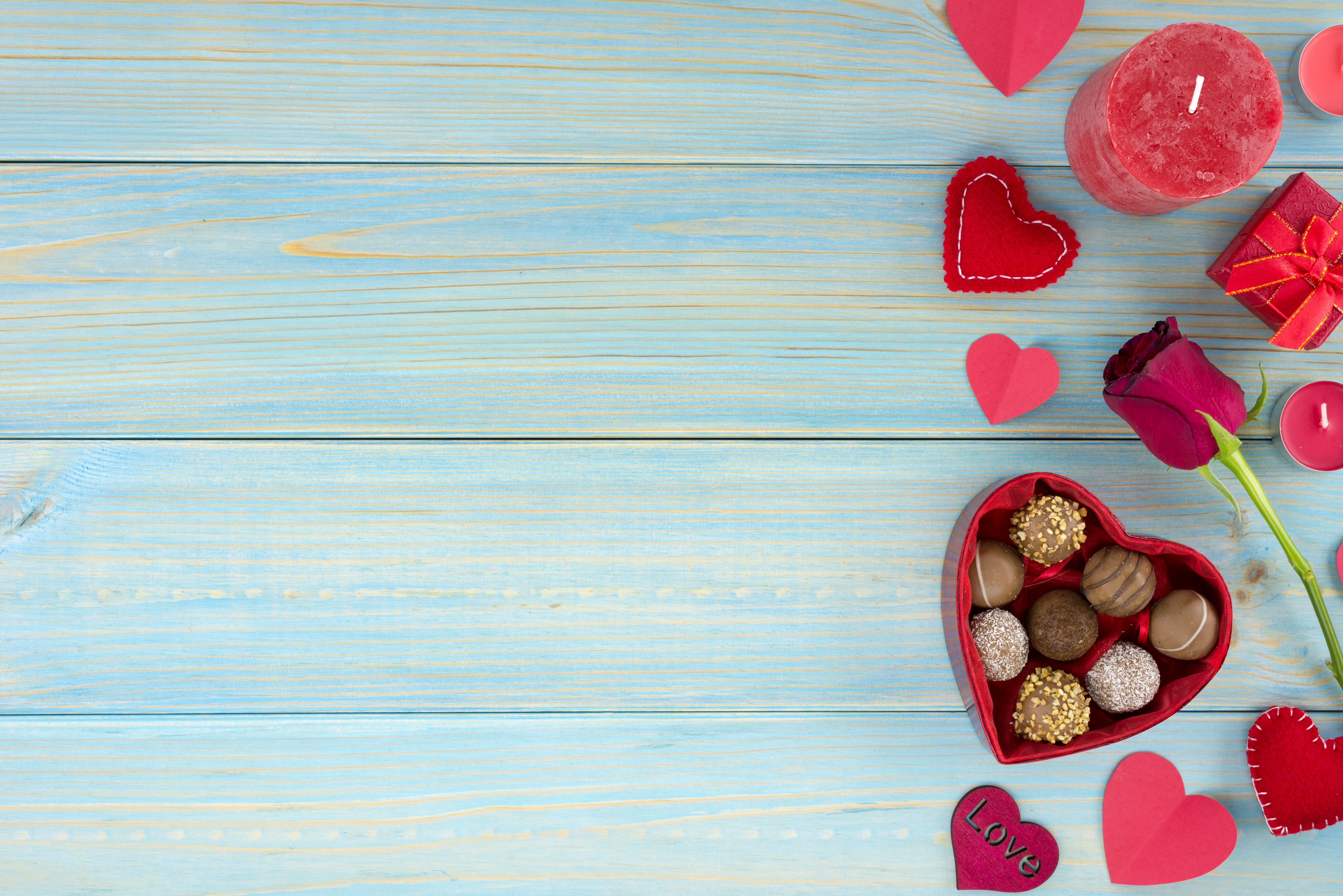 Valentine's Day background with chocolates, rose, candle, and hearts on a blue wooden table
