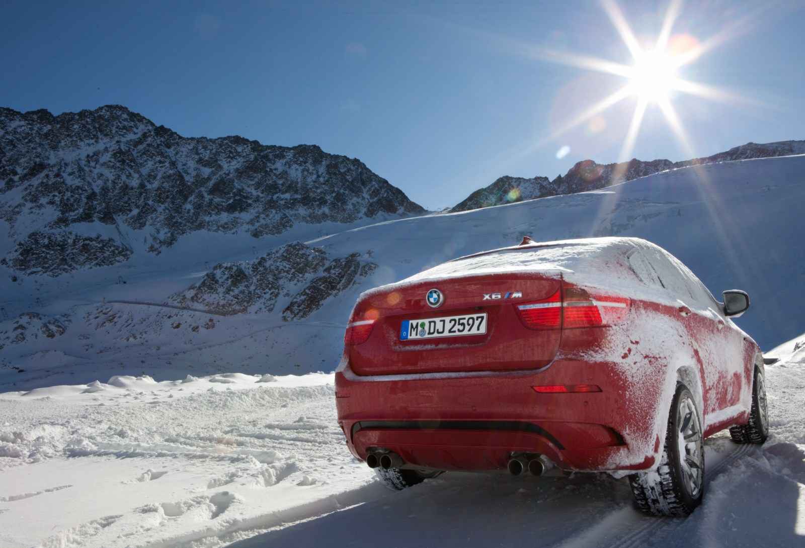 Red BMW X6 M parked in snowy mountain landscape