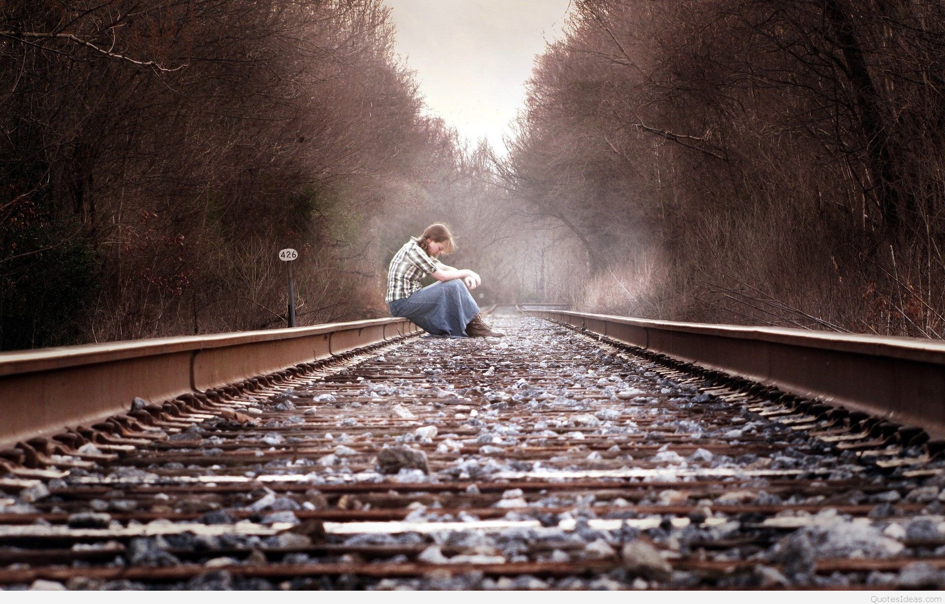 A solitary figure sits hunched over on a railroad track, conveying a sense of sadness and loneliness
